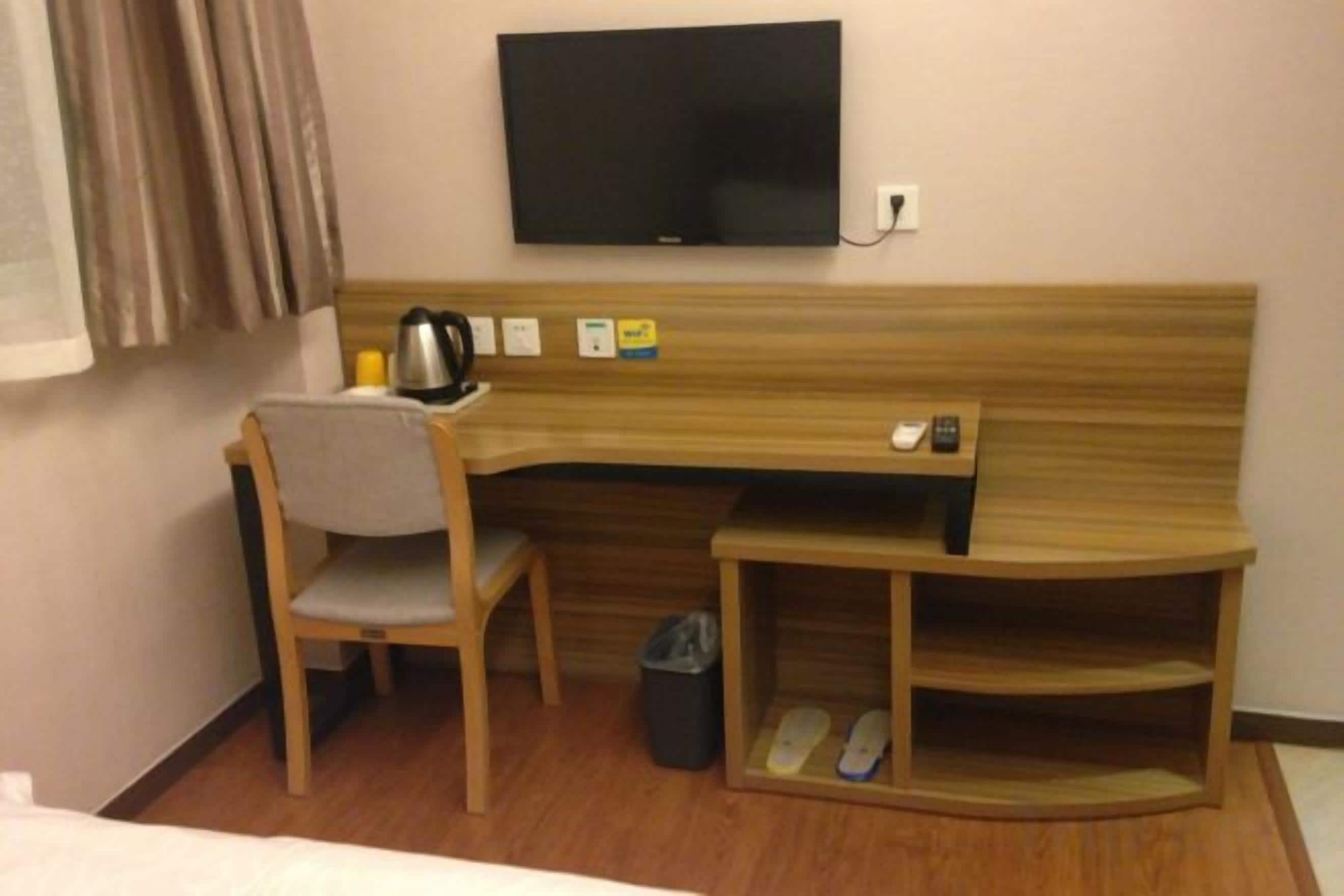 Una camera d'albergo con scrivania, sedia, televisore e un portascarpe.