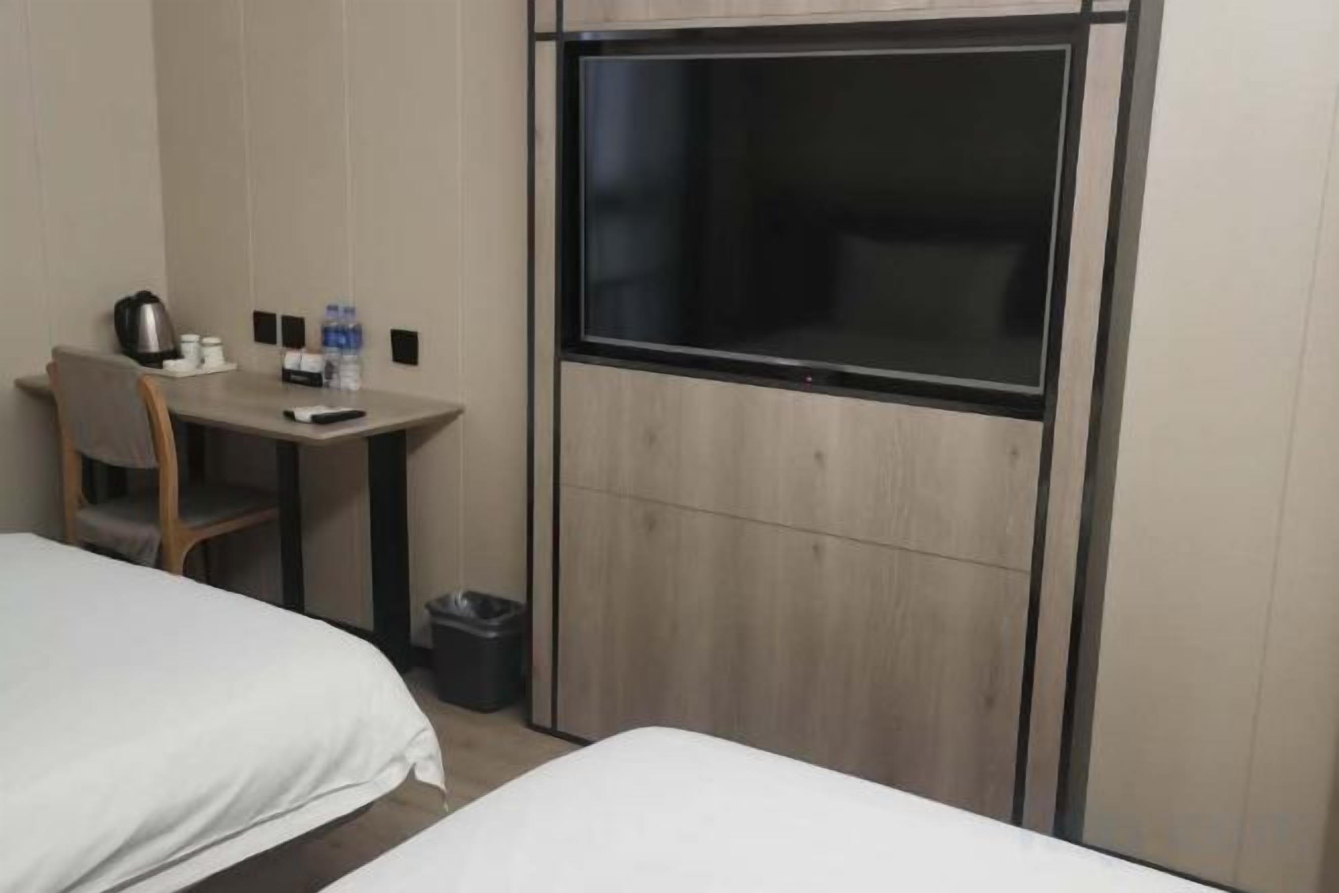 A hotel room with two beds, a desk, a chair, a TV, and a trash bin.