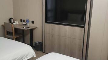 A hotel room with two beds, a desk, a chair, a TV, and a trash bin.