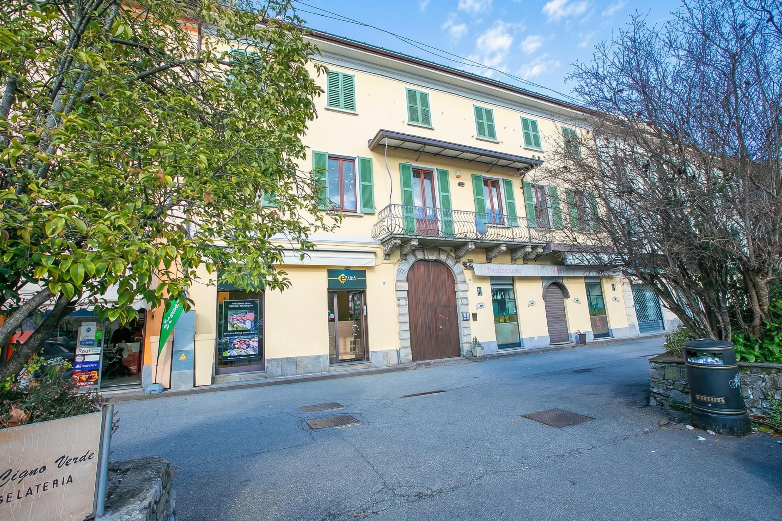 A two-story building with a yellow facade, green shutters, and a central entrance with a large wooden door.