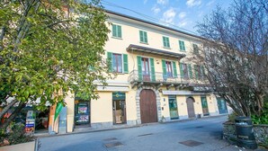 Ein zweistöckiges Gebäude mit gelber Fassade, grünen Fensterläden und einem zentralen Eingang mit einer großen Holztür.