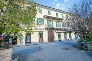 Un bâtiment à deux étages, doté d’une façade jaune, de volets verts et d’une entrée centrale avec une grande porte en bois.