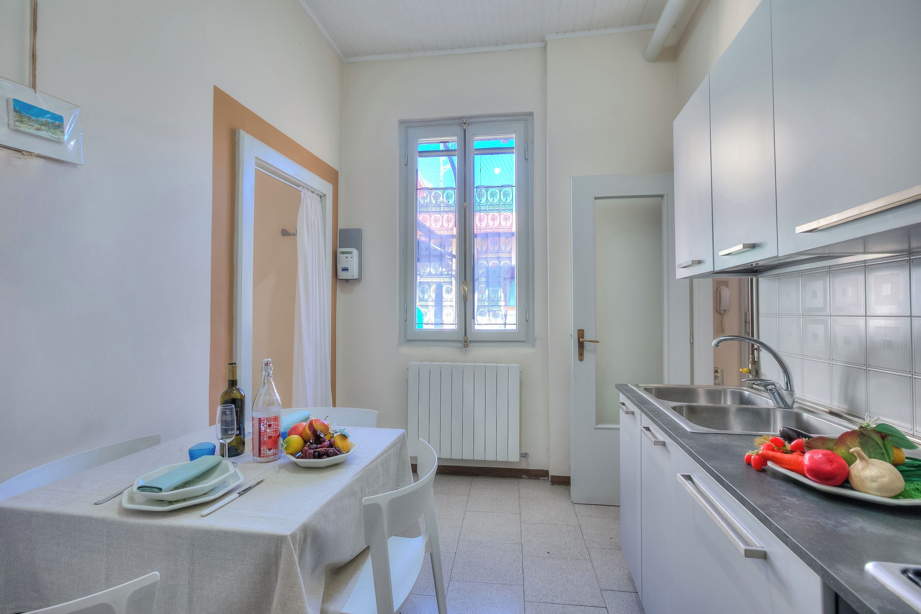Una cucina compatta con tavolo da pranzo, mobili bianchi, una finestra vista e un lavandino.