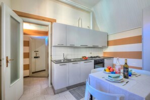 A modern kitchen with white cabinets, a gas stove, and a dining area with a table set for two. - Apt. Gabriella: Studio in the Centre of Laveno (Laveno Mombello)