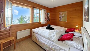 Ein Schlafzimmer mit Holzvertäfelung, einem großen Bett, einem Nachttisch, einem Heizkörper und einem Fenster mit Vorhängen.