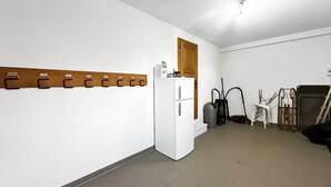 Ein kleiner, sauberer Raum mit einem weißen Kühlschrank, einem hölzernen Kleiderständer und einer Mülltonne.