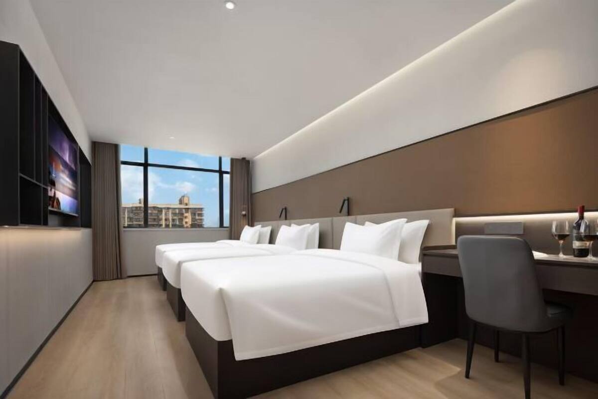 Quarto de hotel moderno com uma cama grande, uma mesa e vista para a cidade.
