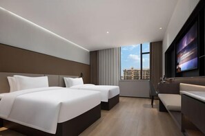 Une chambre d’hôtel moderne dotée de deux lits, d’un coin salon, d’une télévision et d’une grande fenêtre donnant sur la ville.