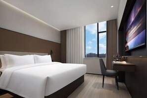 Une chambre d’hôtel moderne, dotée d’un grand lit, d’un bureau, d’une chaise et d’un téléviseur fixé au mur.