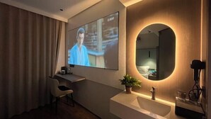 A modern hotel room with a flat-screen TV mounted on the wall, a round mirror, a desk with a chair, a sink, and a potted plant. - mutai Hotel Changsha (Changsha)