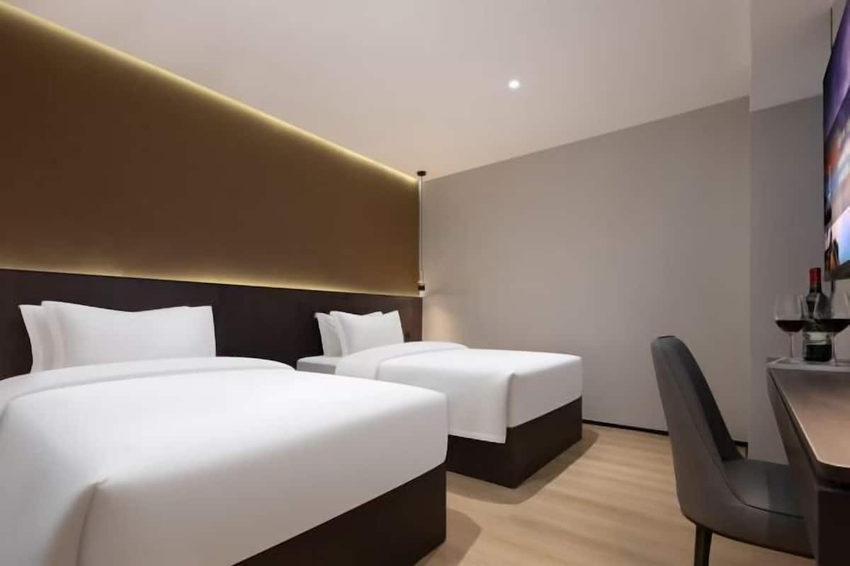 Quarto de hotel com duas camas, uma mesa e uma cadeira.