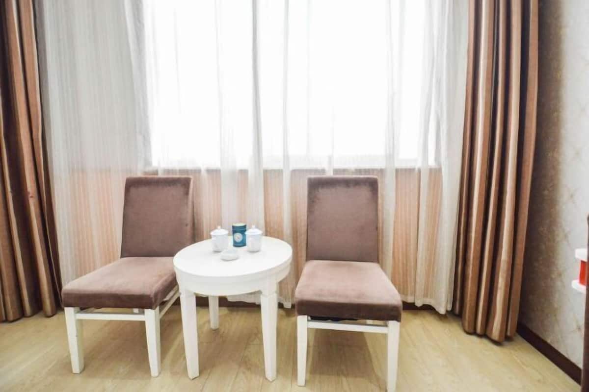 Quarto com duas cadeiras e uma pequena mesa redonda, cortinas e uma janela.