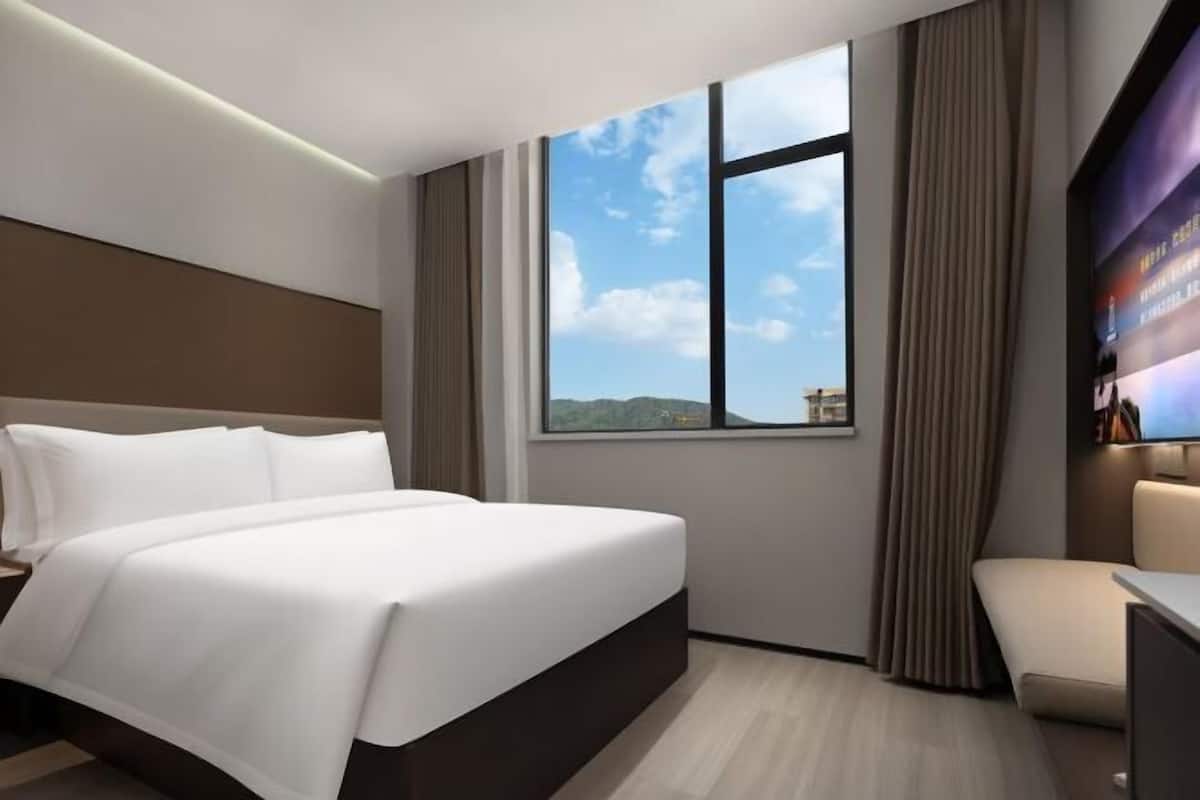 Quarto de hotel com uma cama grande, televisão e janela vista para a cidade.