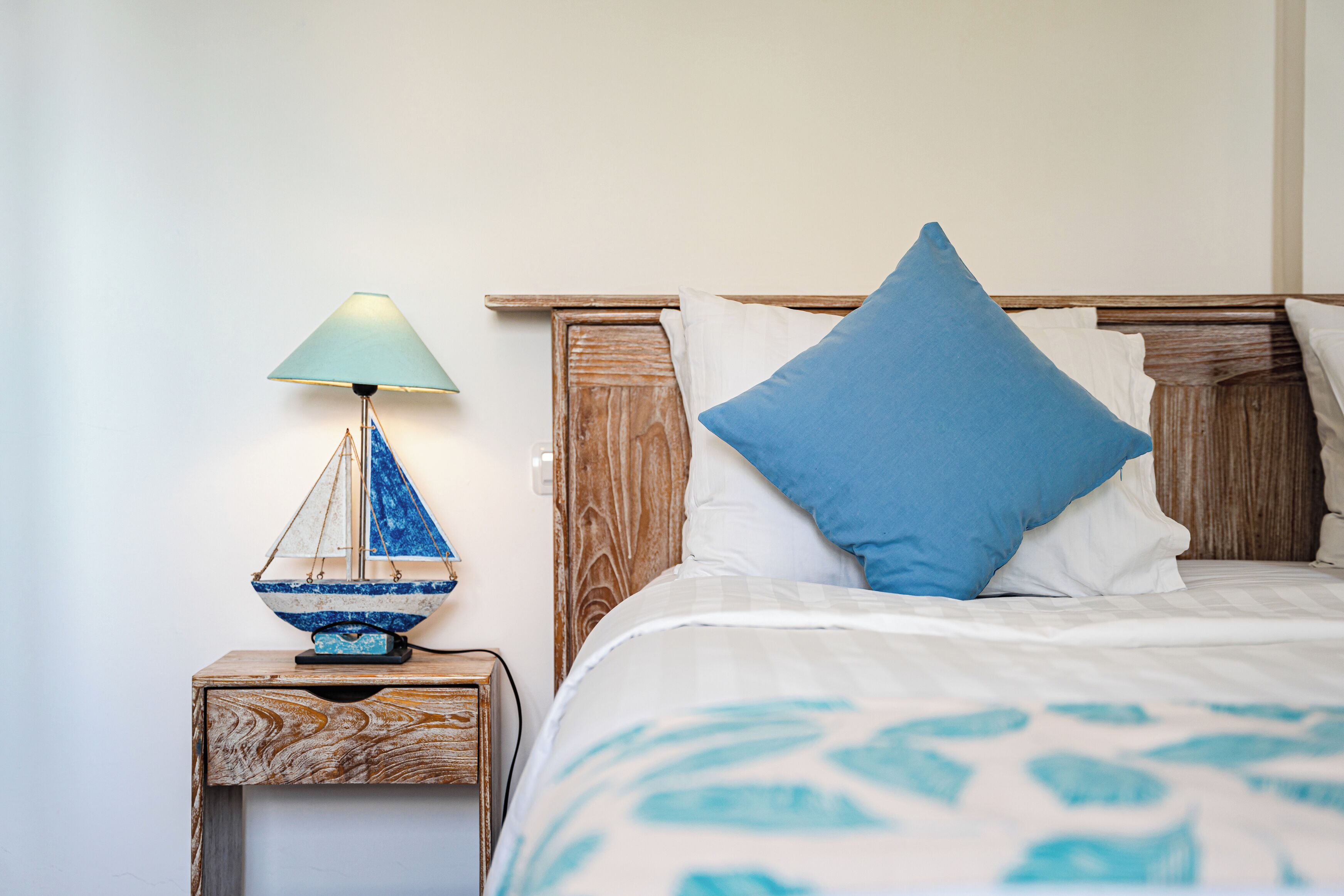 A bed with a blue pillow, a wooden nightstand with a blue and white lamp, and a wooden headboard.