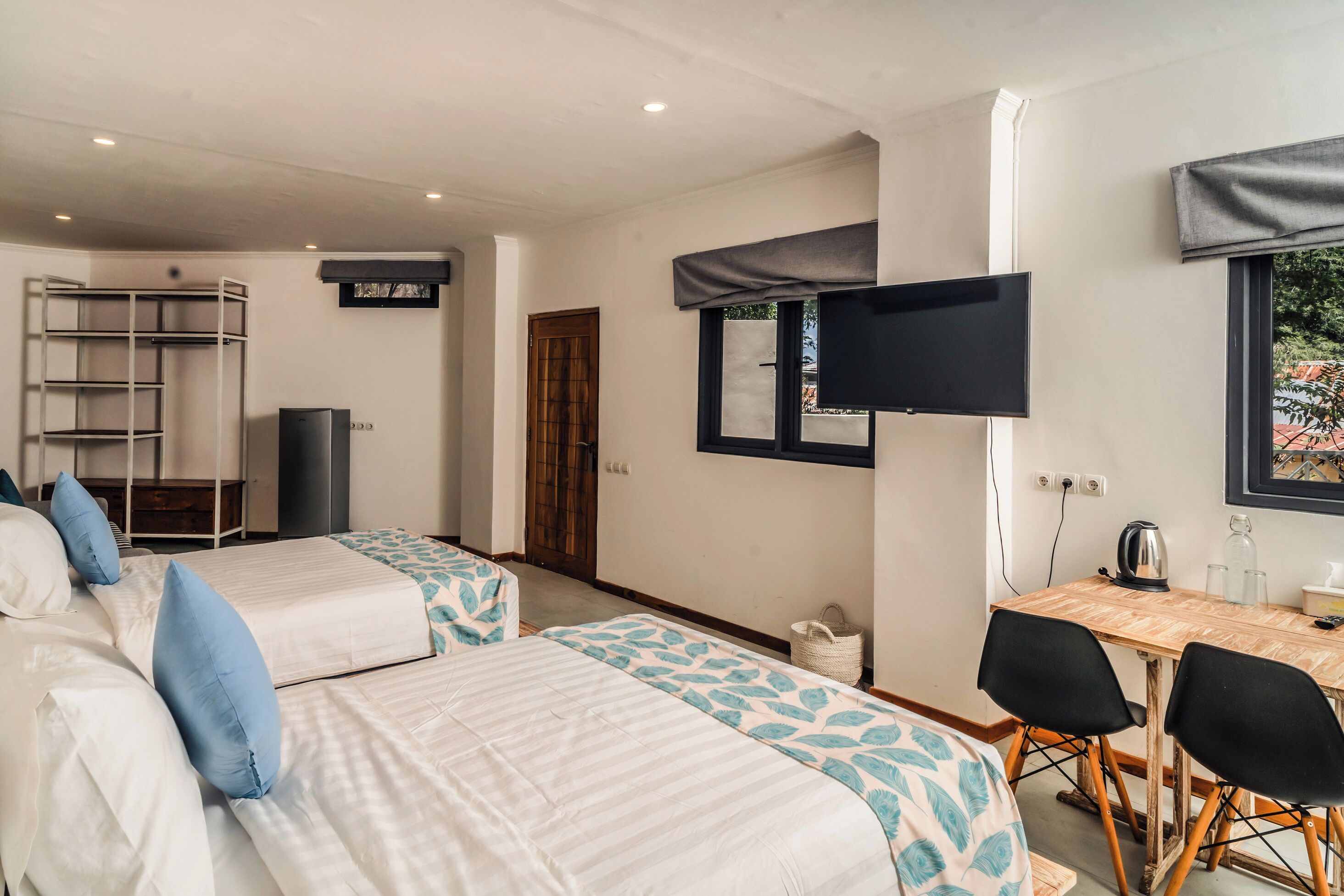 A room with two beds, a desk, chairs, a TV, and a window.