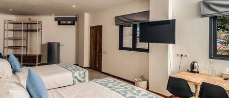 Una habitación con dos camas, un escritorio, sillas, un televisor y una ventana.