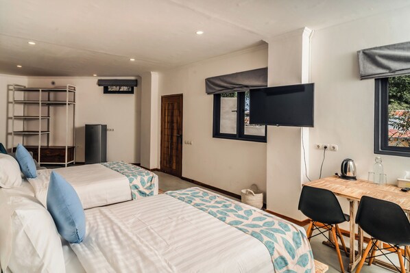 A room with two beds, a desk, chairs, a TV, and a window. - Komodo Suites Downtown (Labuan Bajo)