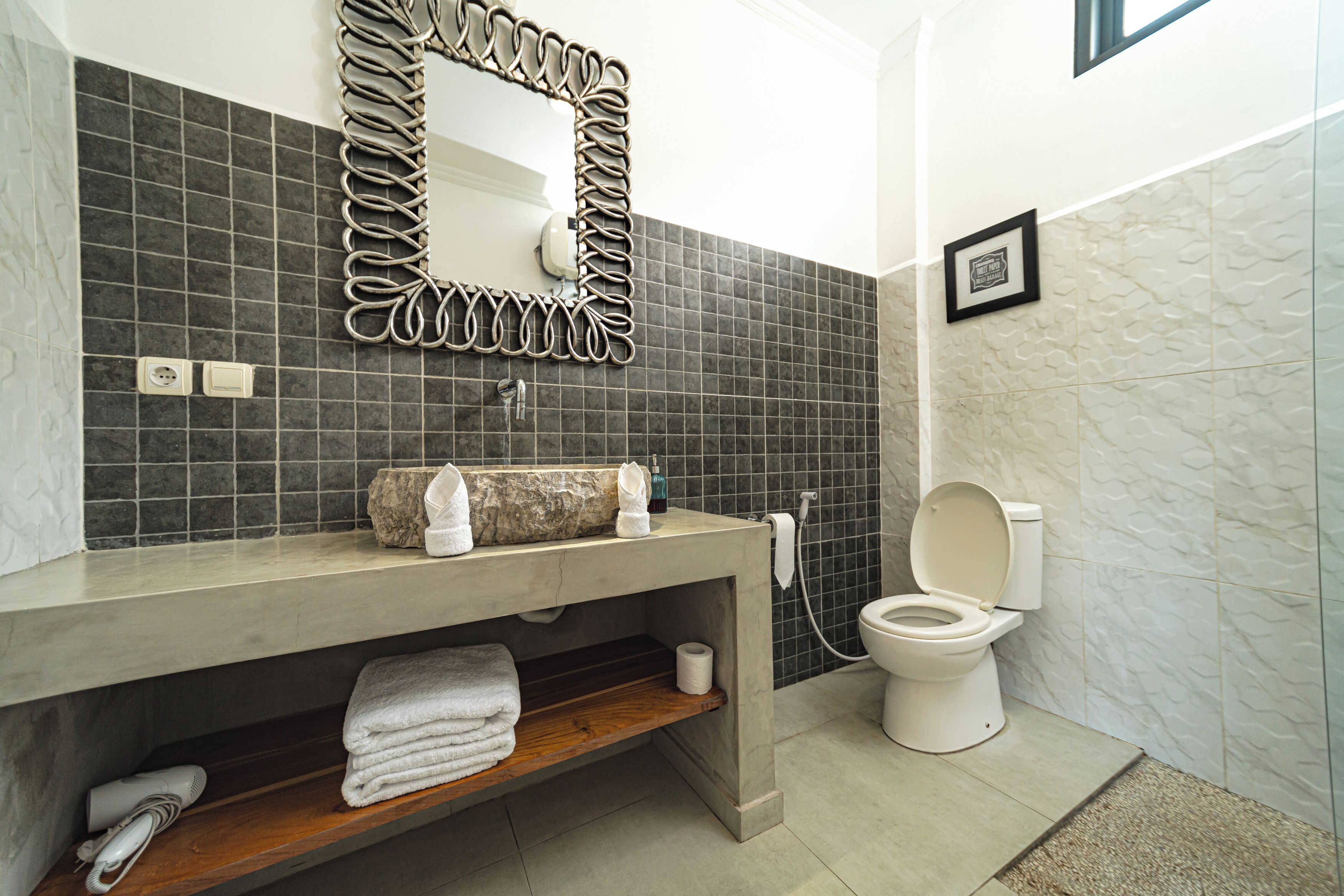 A bathroom with a modern design, featuring a concrete sink, a large mirror with a unique frame, a toilet, and a shower area.