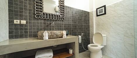 A bathroom with a modern design, featuring a concrete sink, a large mirror with a unique frame, a toilet, and a shower area.