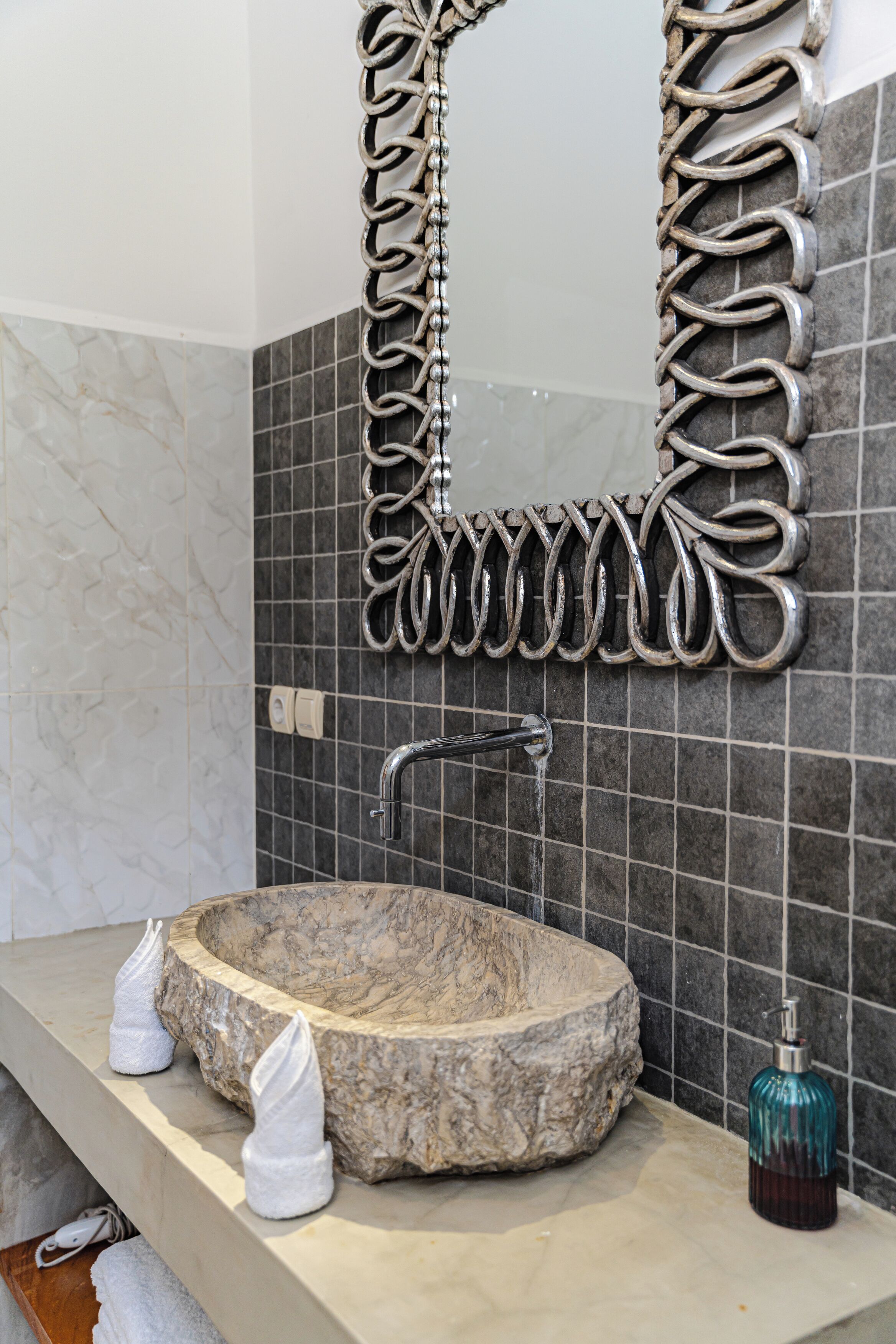 A bathroom with a round stone sink, a decorative mirror frame, and a soap dispenser.