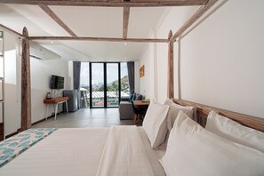A bedroom with a large bed, a desk, and a view of the outdoors. - Komodo Suites Downtown (Labuan Bajo)