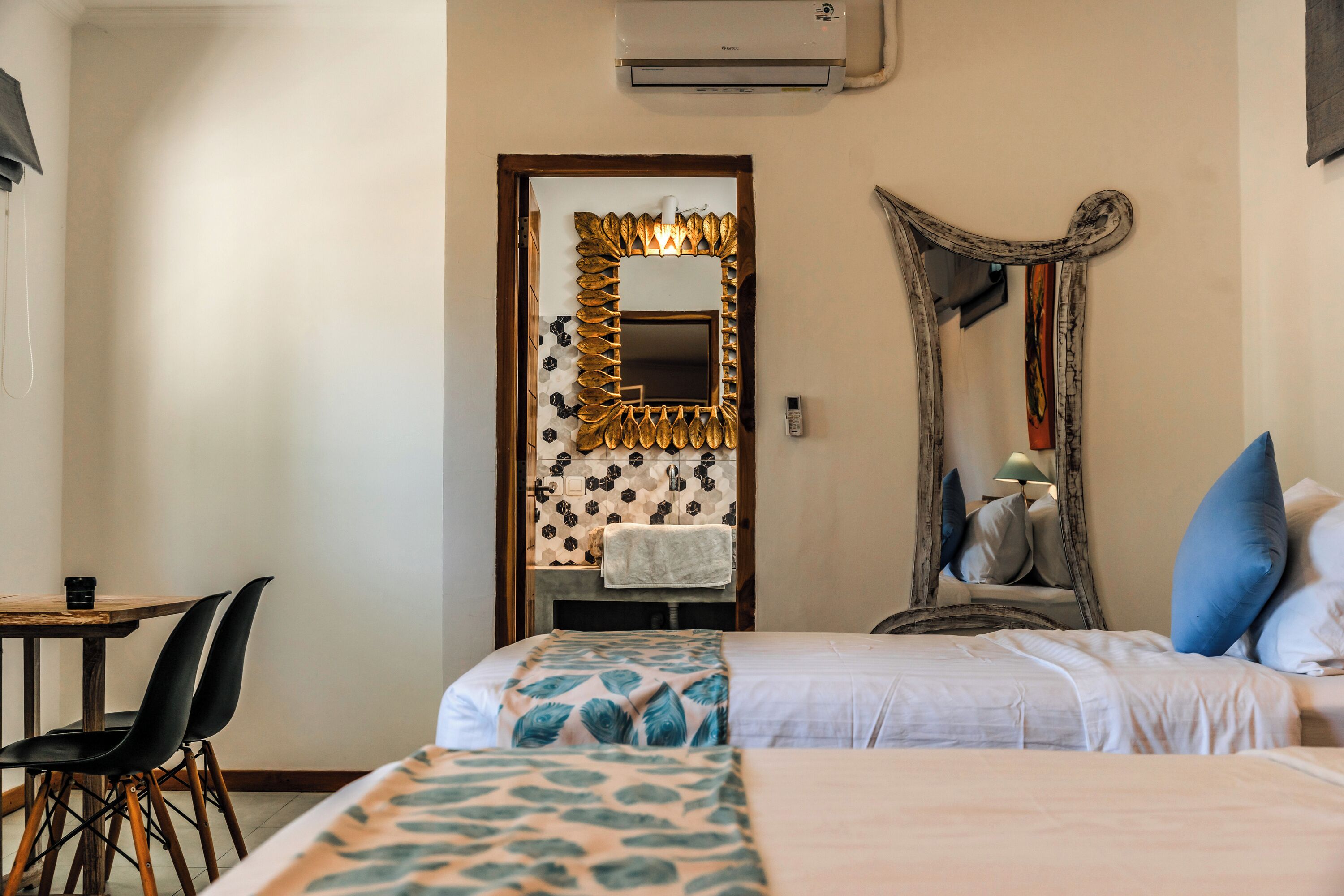 Een hotelkamer met twee bedden, een houten tafel met stoelen, een spiegel en een wandairconditioner.