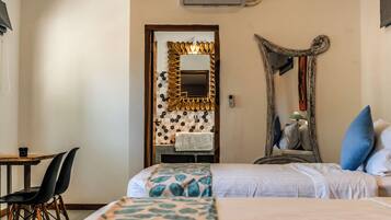 A hotel room with two beds, a wooden table with chairs, a mirror, and a wall-mounted air conditioner.