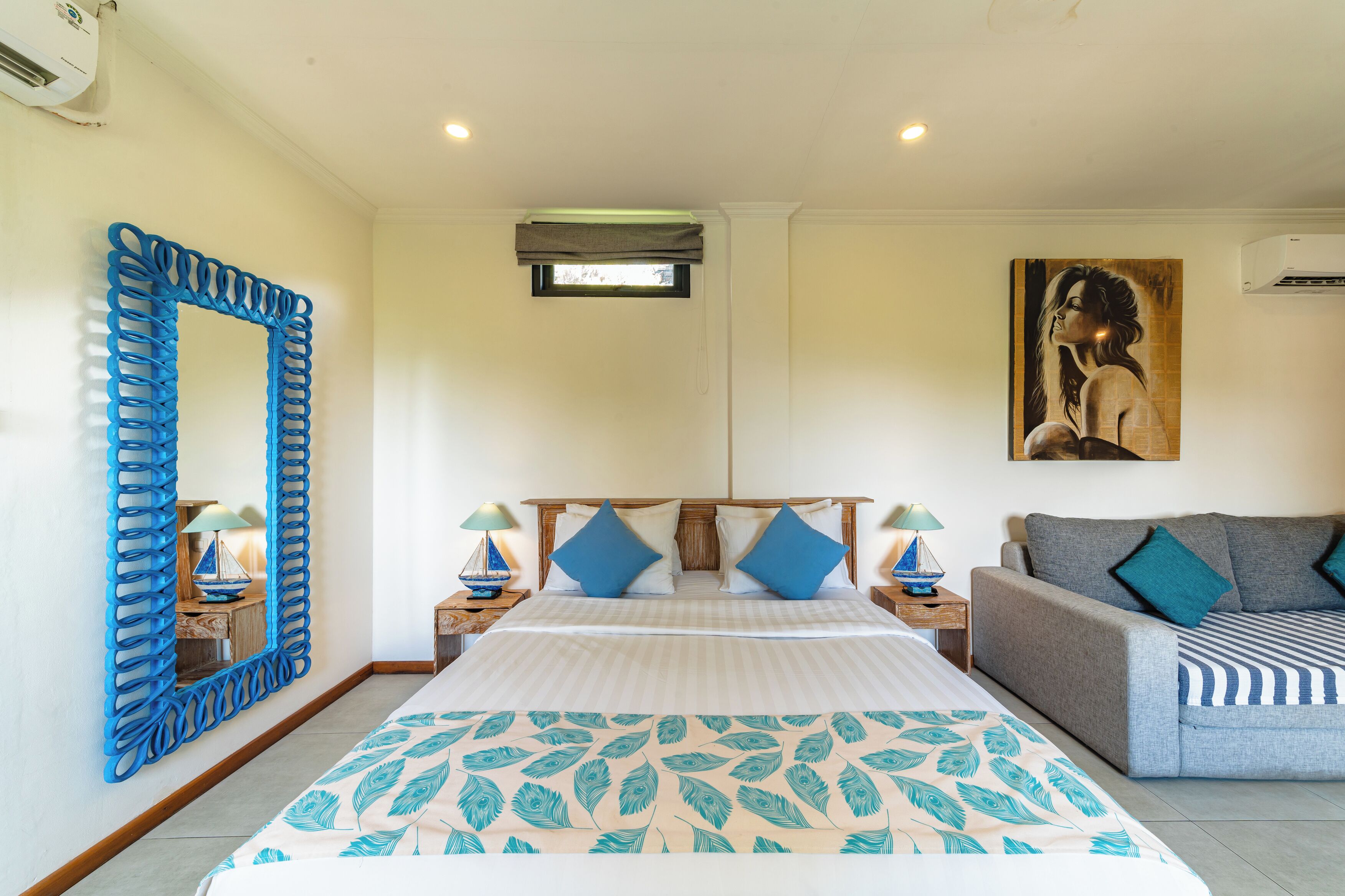 A bedroom with a large bed, a sofa, a decorative mirror, and a painting on the wall.