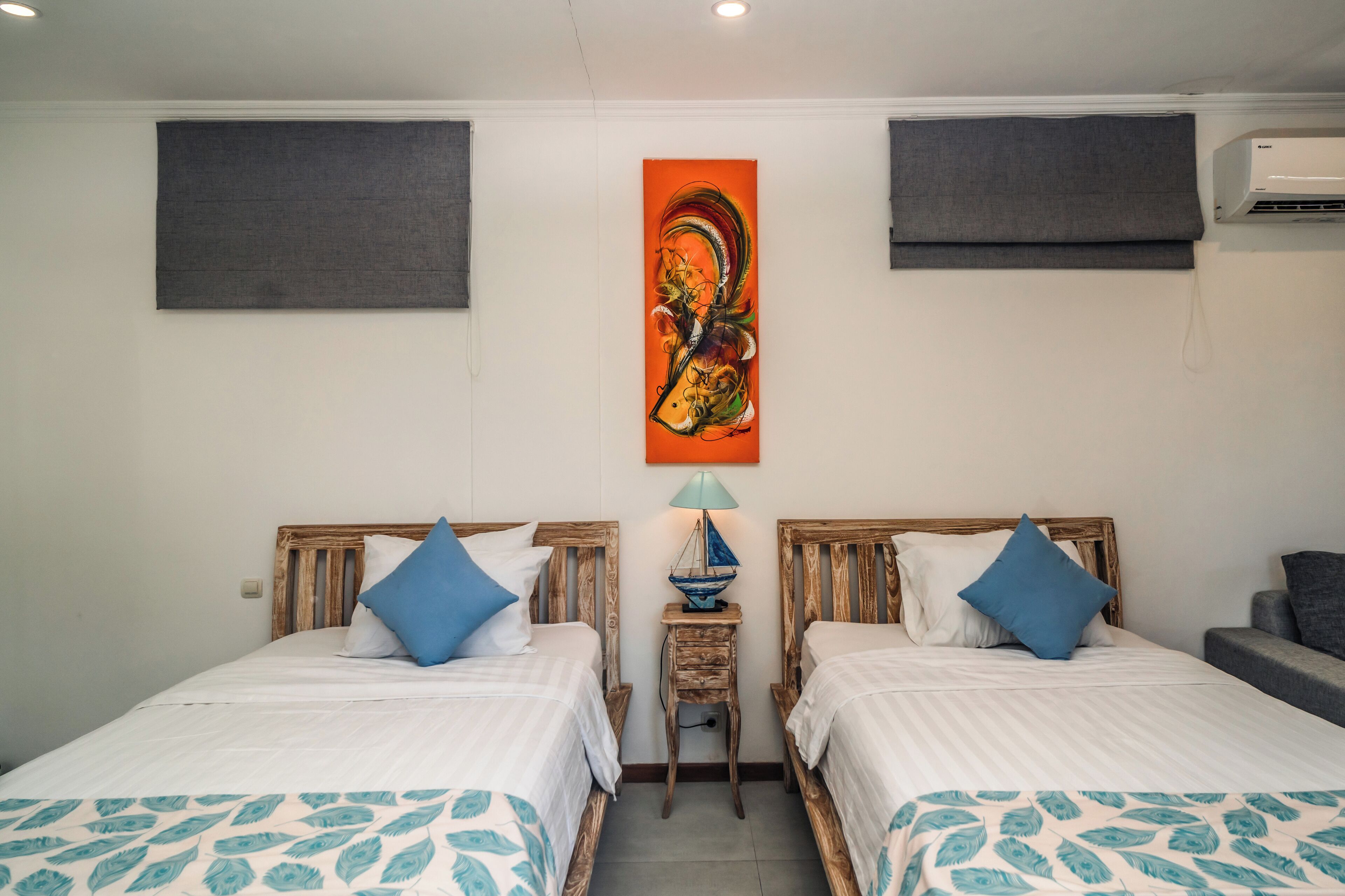 A hotel room with two beds, a nightstand with a lamp, and a wall-mounted air conditioner.