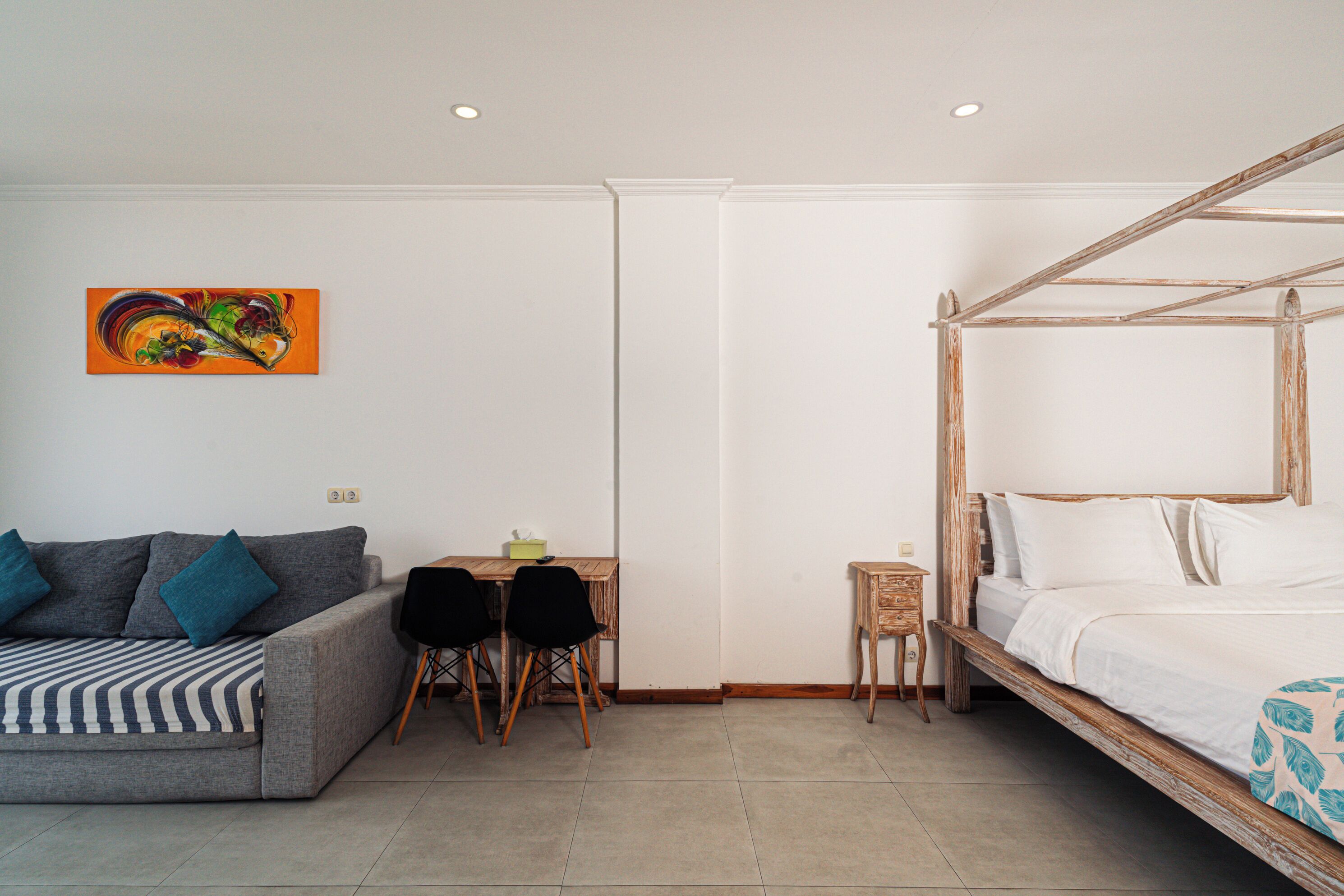 Una habitación con cama, sofá, una mesita con sillas y un cuadro en la pared.