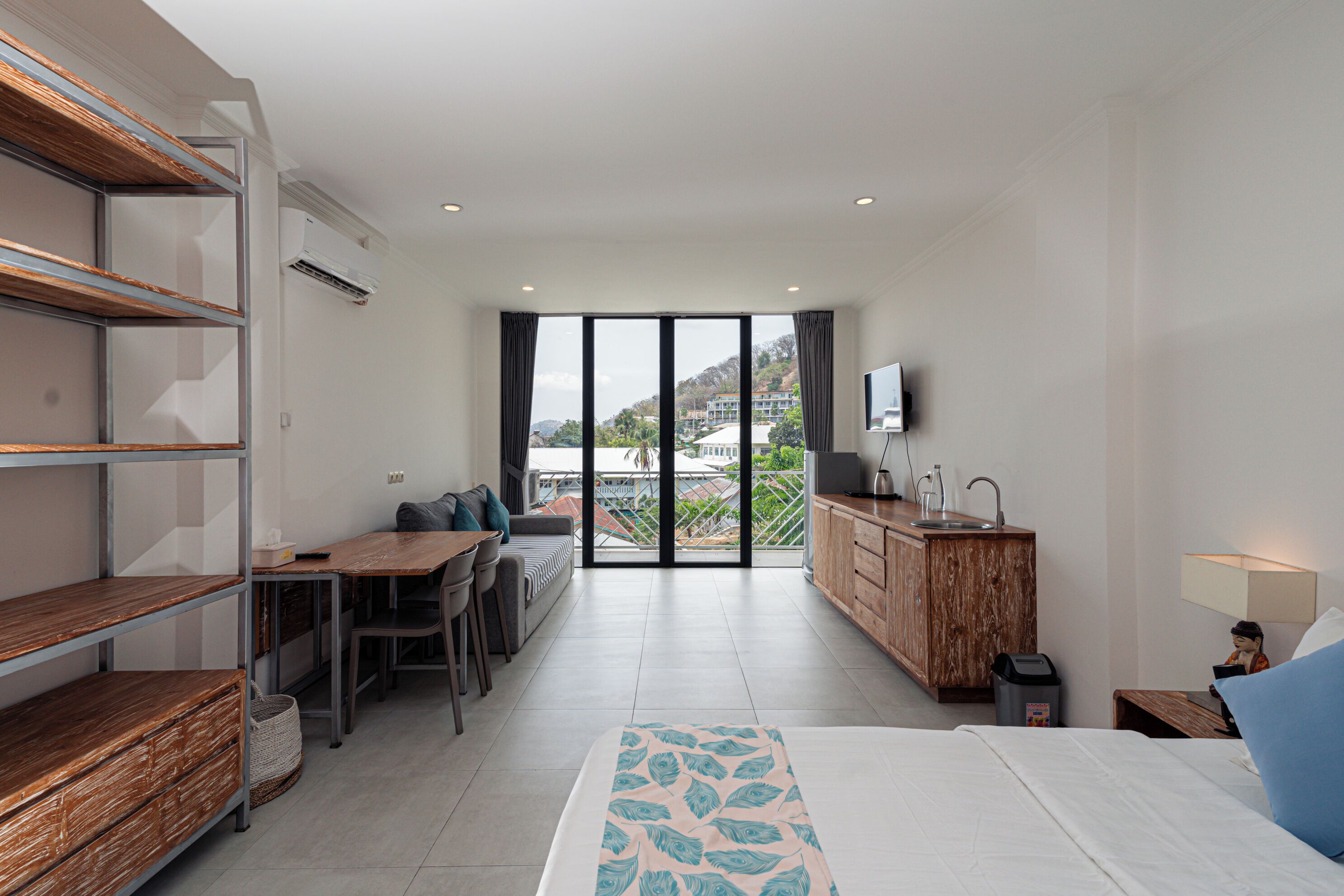 A modern hotel room with a bed, a desk, a sofa, and a balcony with a view of the city.