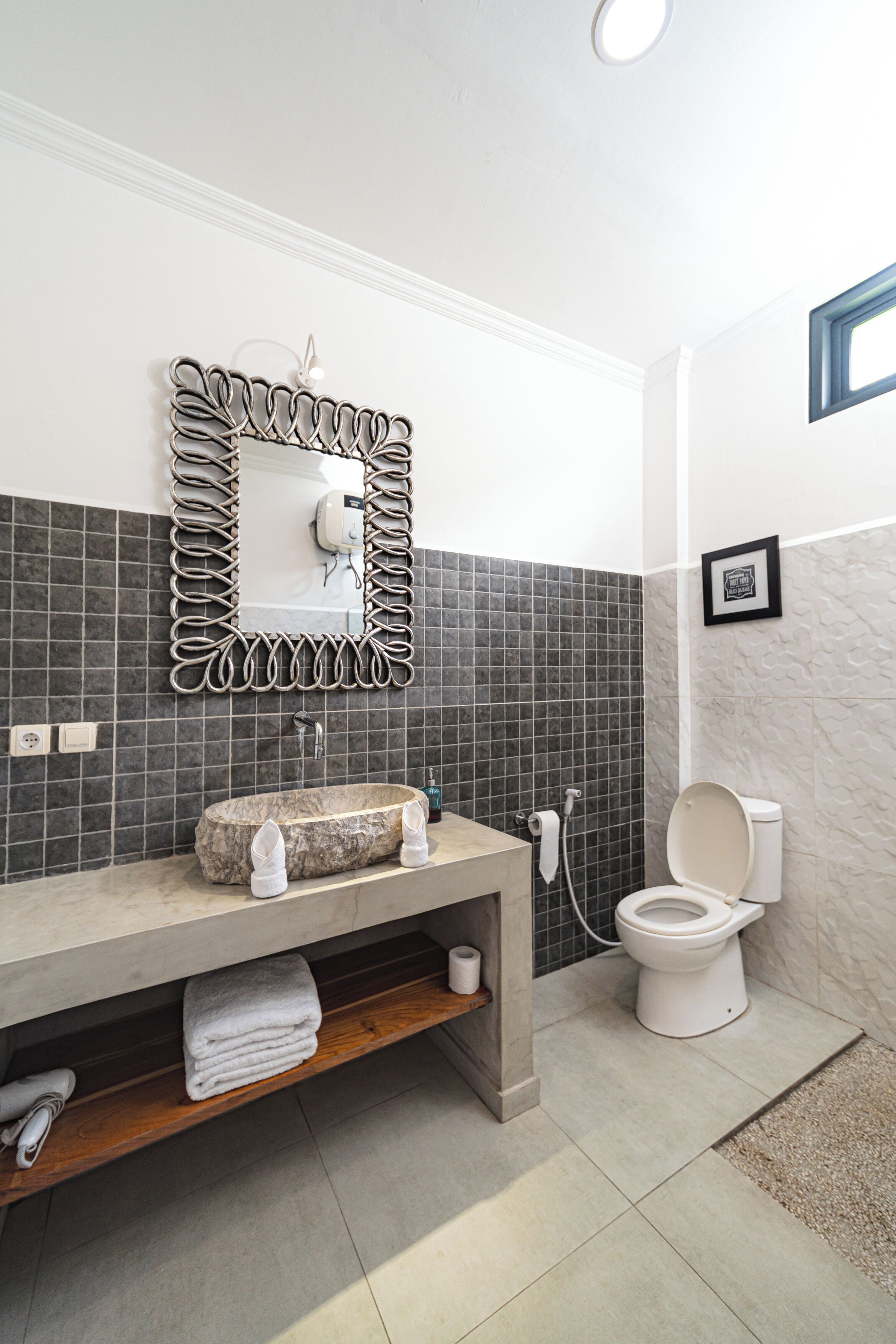 A modern bathroom with a marble sink, a freestanding toilet, a towel rack, and a mirror with a decorative frame.