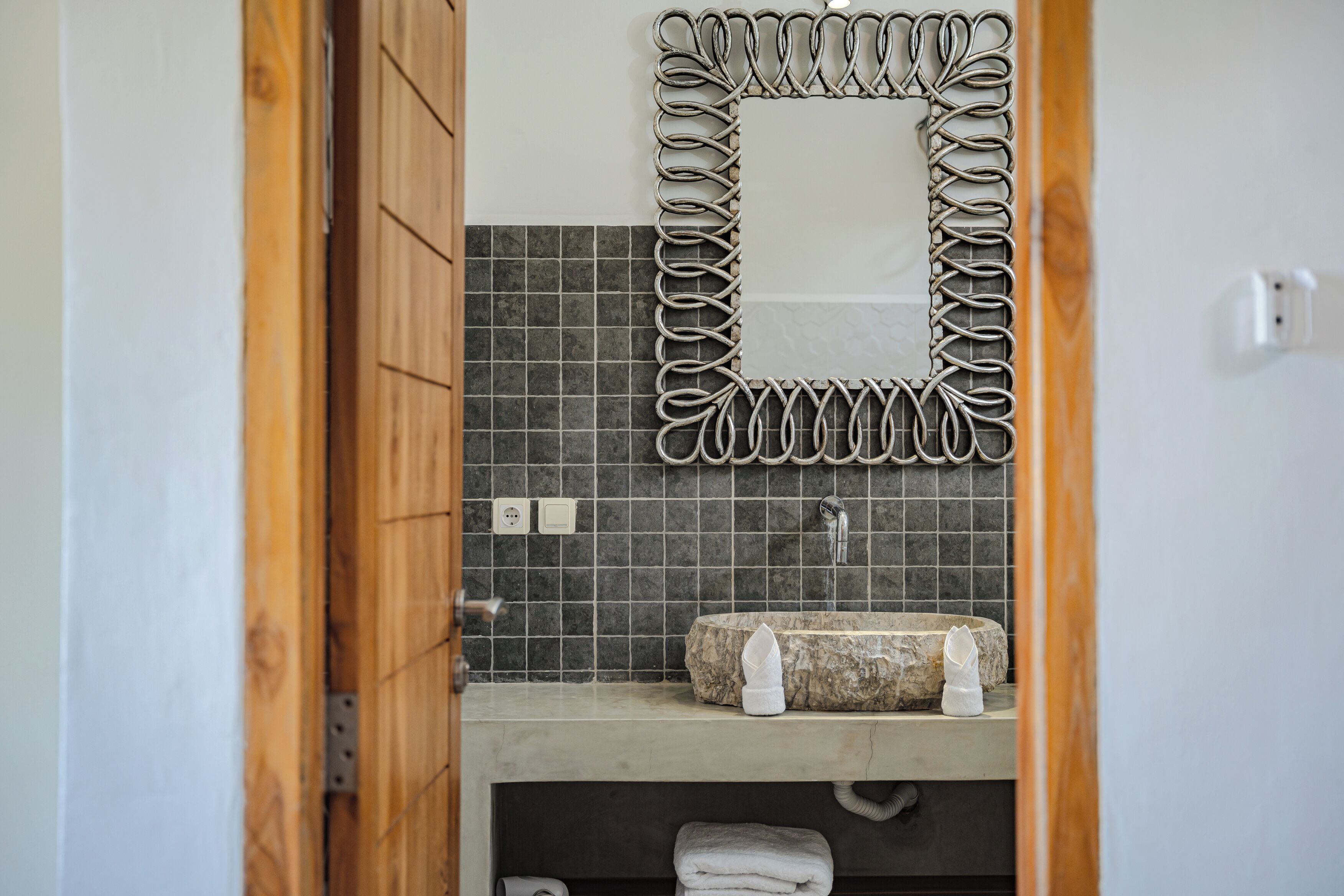 A bathroom with a stone sink, a mirror with a metal frame, and a tiled backsplash.