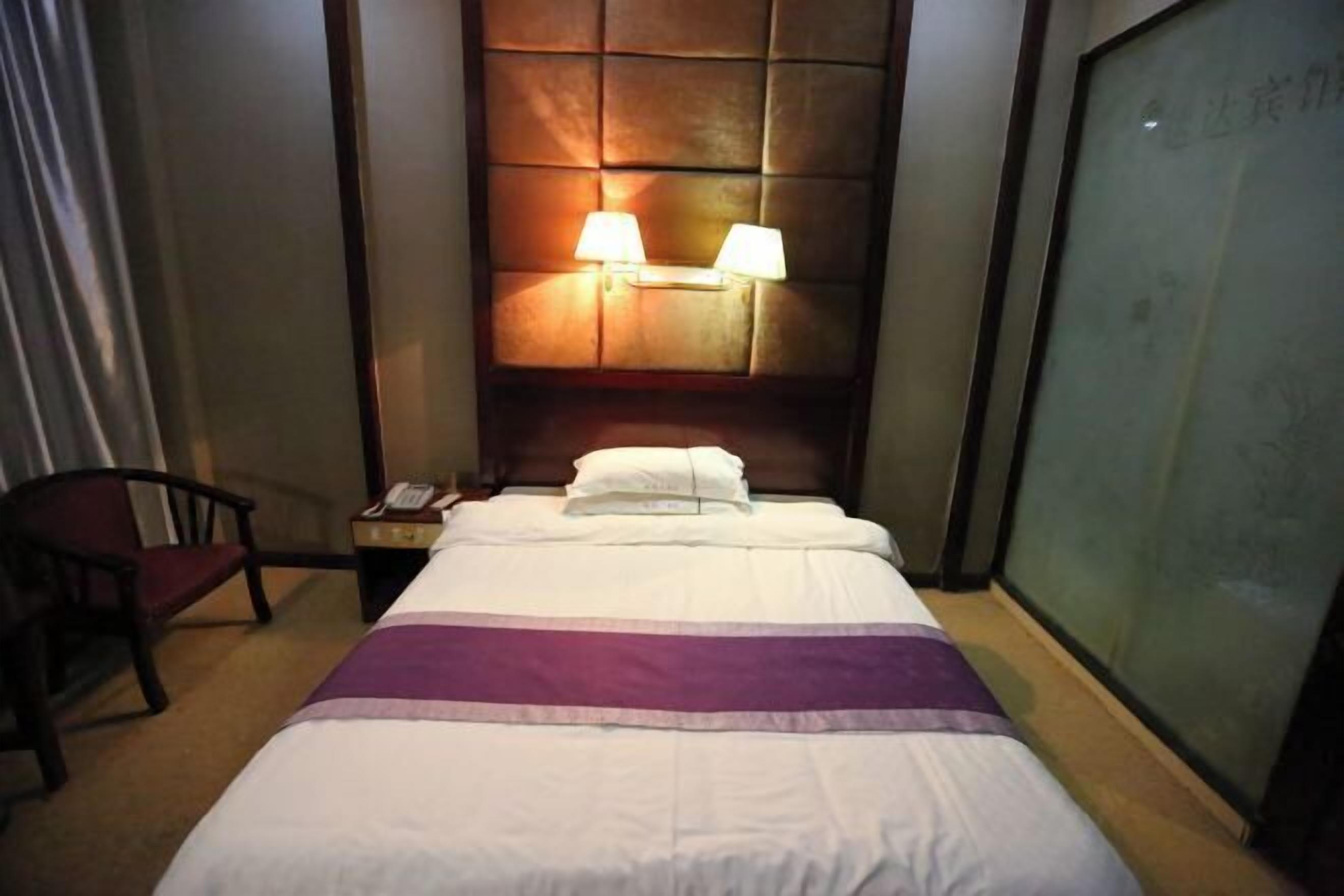 A hotel room with a bed, two bedside lamps, a chair, and a nightstand with a phone.