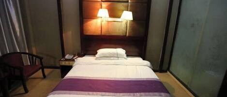 A hotel room with a bed, two bedside lamps, a chair, and a nightstand with a phone.