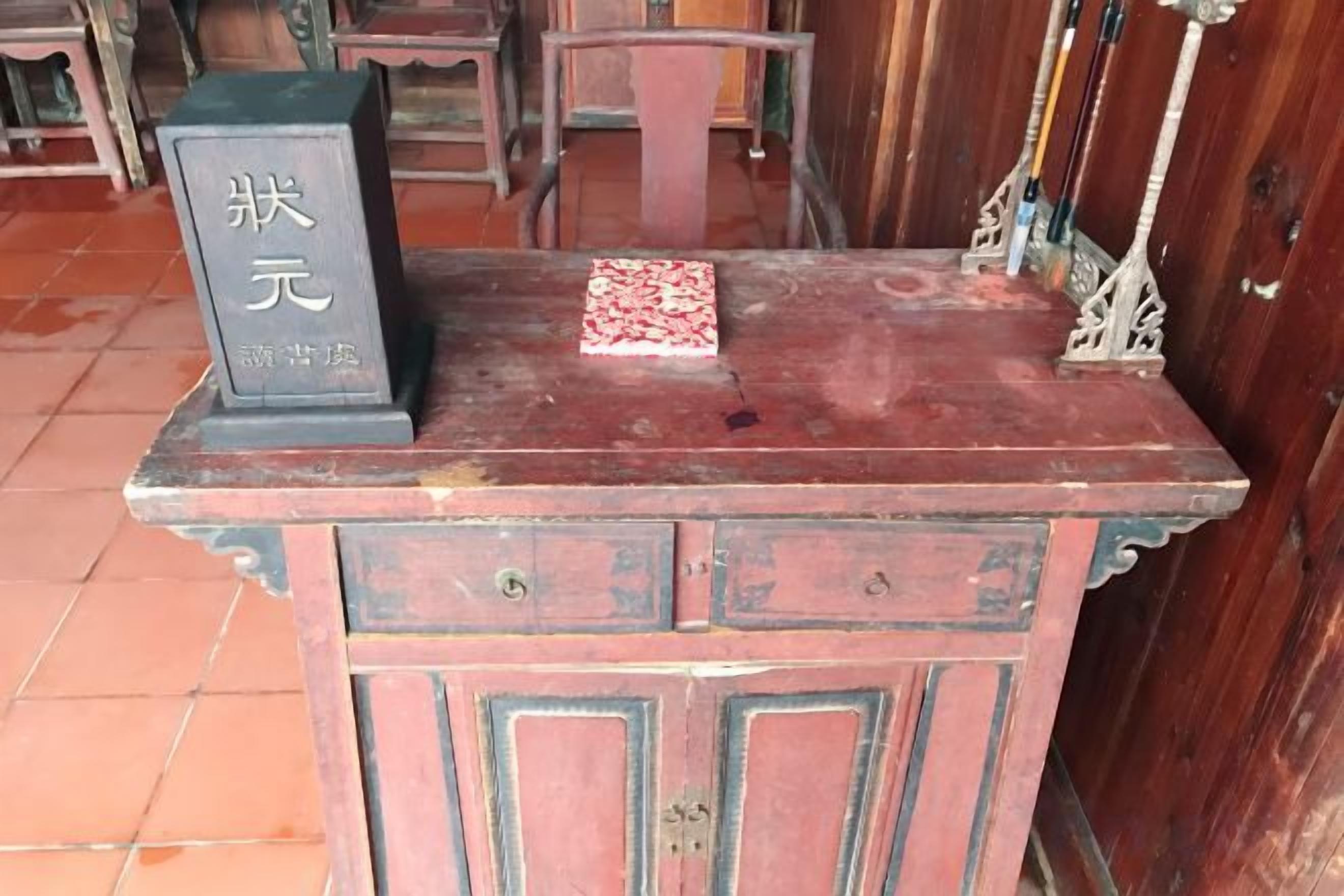Una mesa de madera con una placa, un adorno pequeño y un cajón.