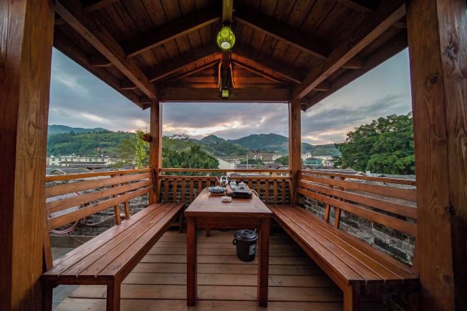 A wooden deck with benches and a table, overlooking a river and mountains.