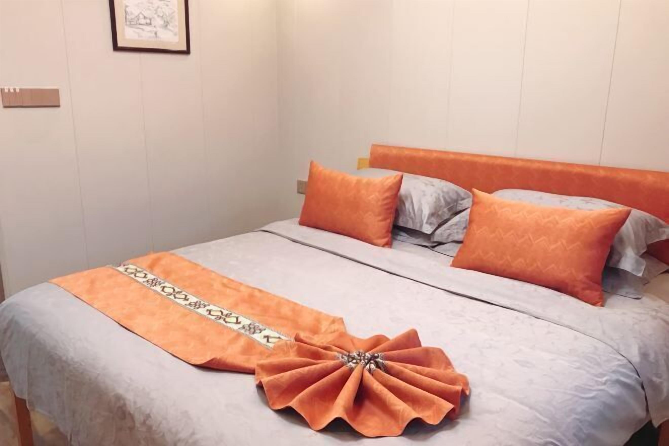 Una cama bien hecha con ropa de cama naranja y una toalla decorativa color naranja.