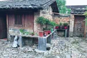 Un patio rústico con suelo de piedra, estructuras de madera y plantas en macetas.