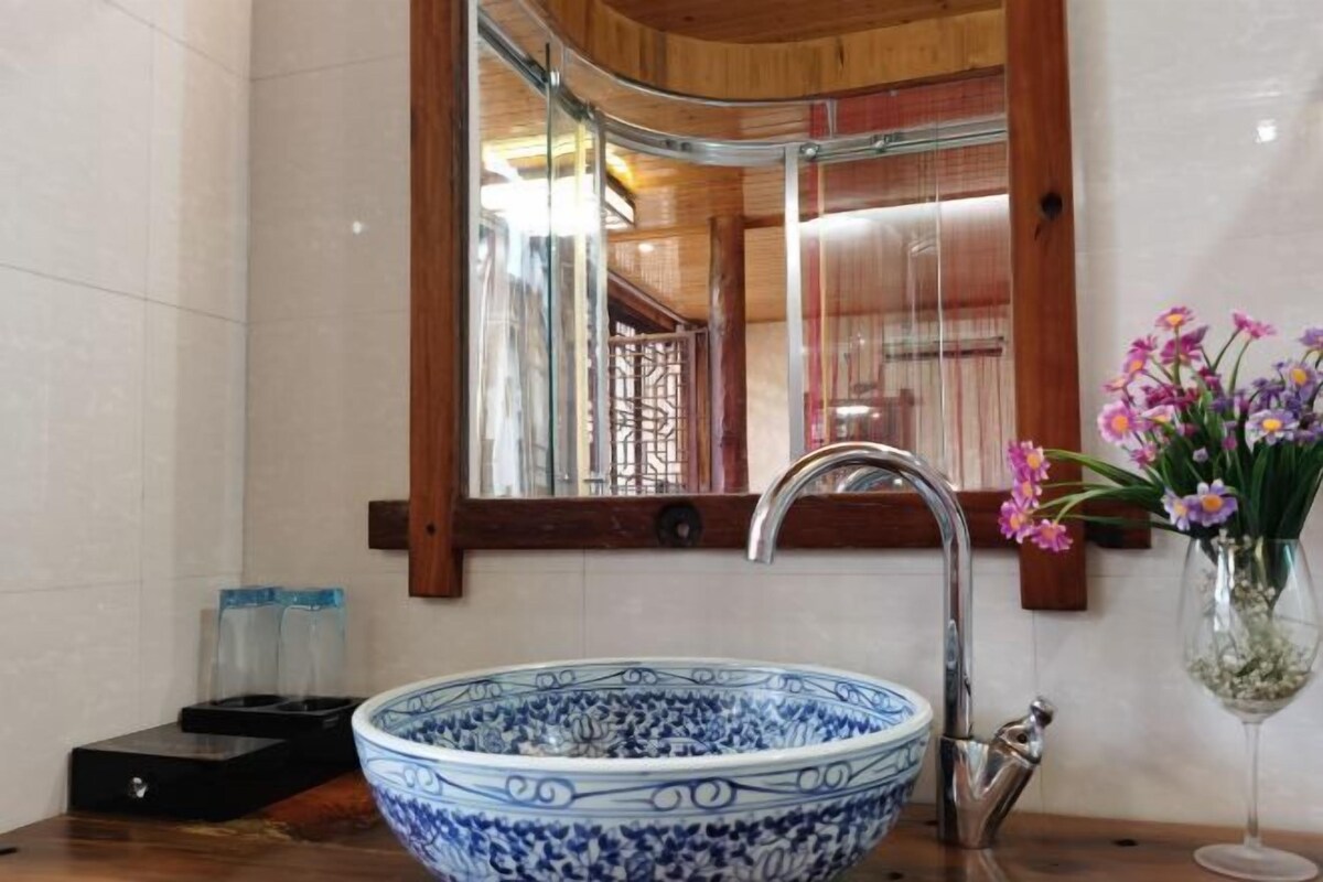 A bathroom with a large blue and white ceramic sink, a modern faucet, a mirror, and a vase with flowers.
