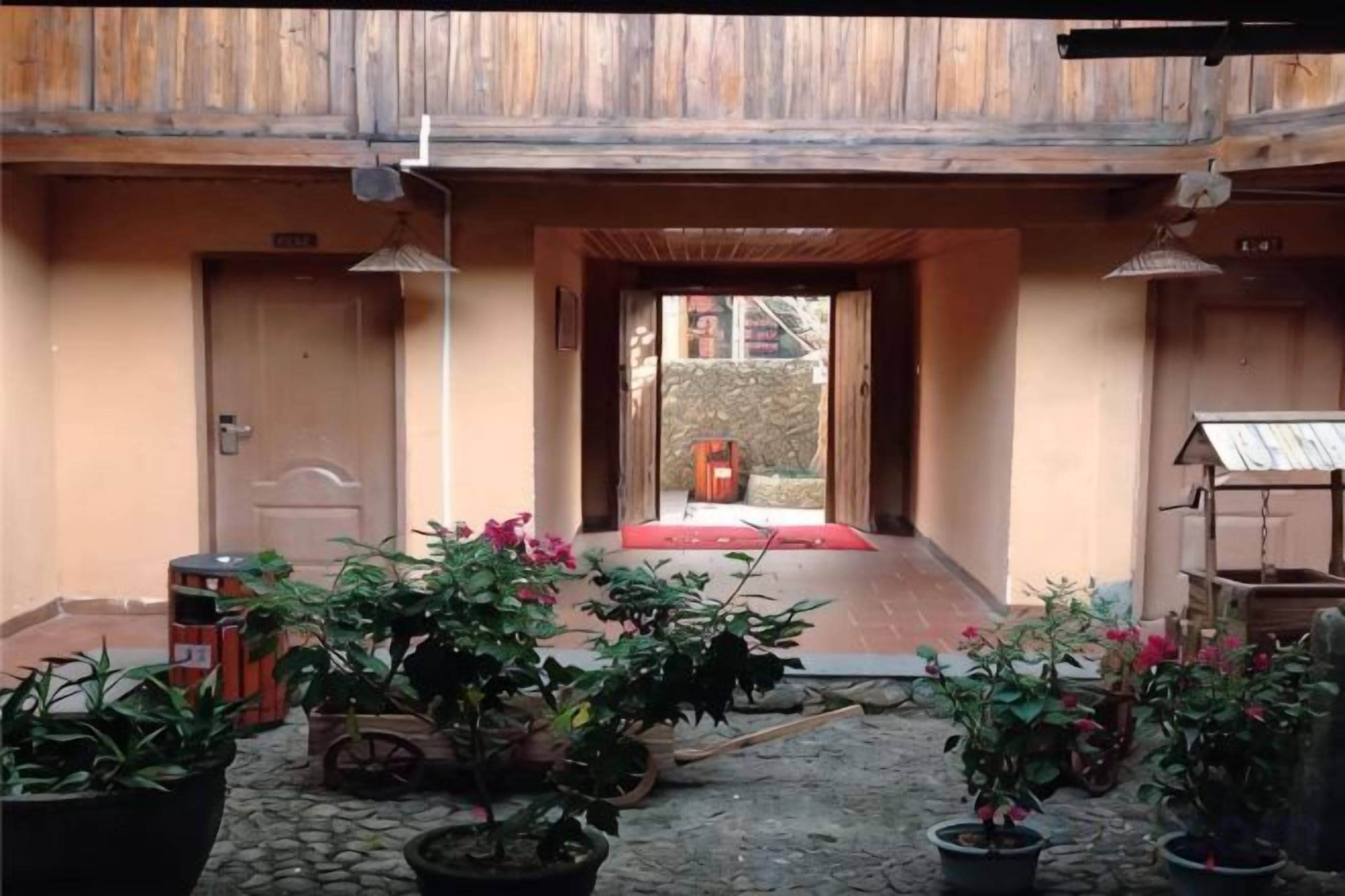 A courtyard with potted plants, a wooden door, and a red mat leading to a room.