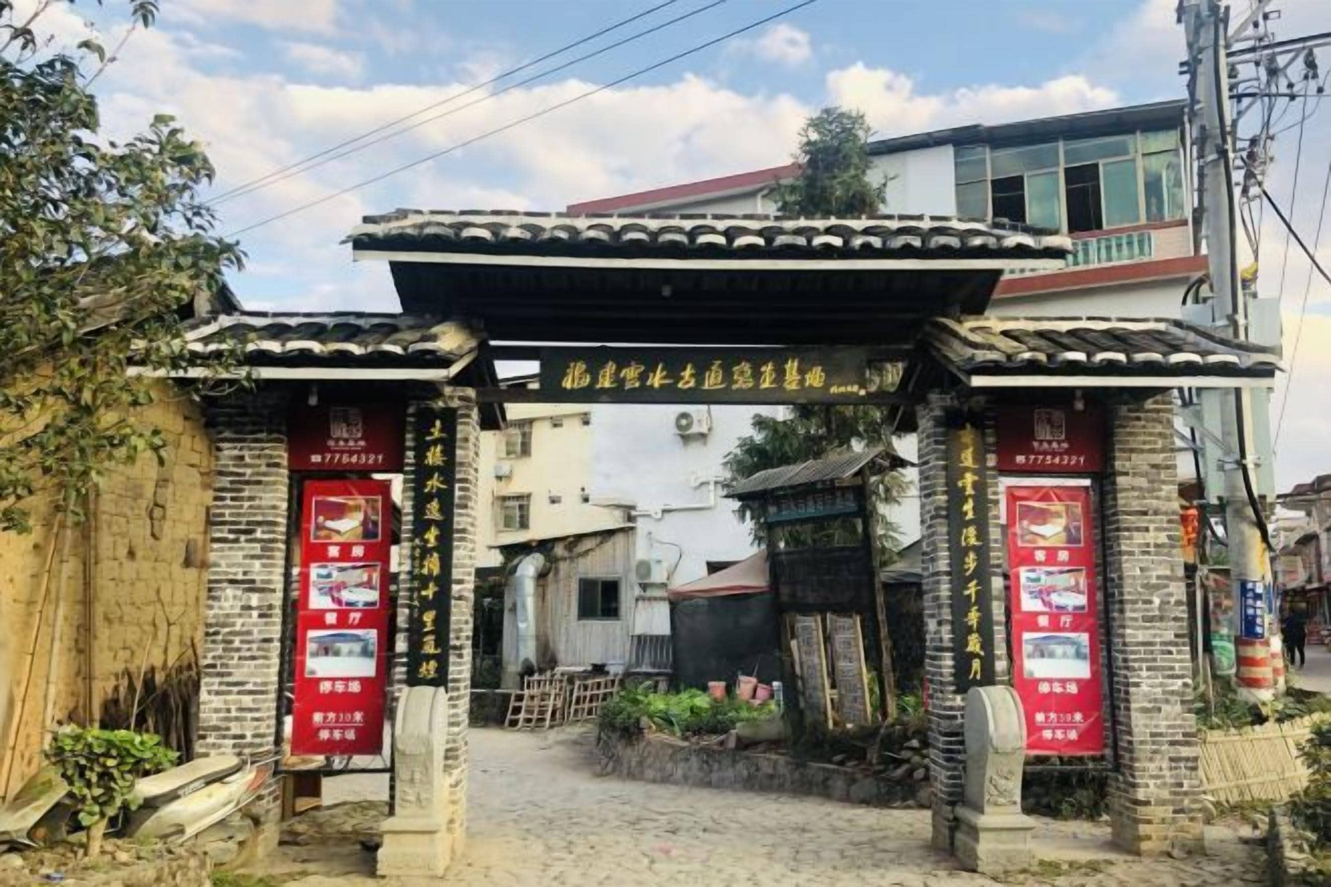 A traditional Chinese gate with a red banner, leading to a building with a tiled roof and a balcony.