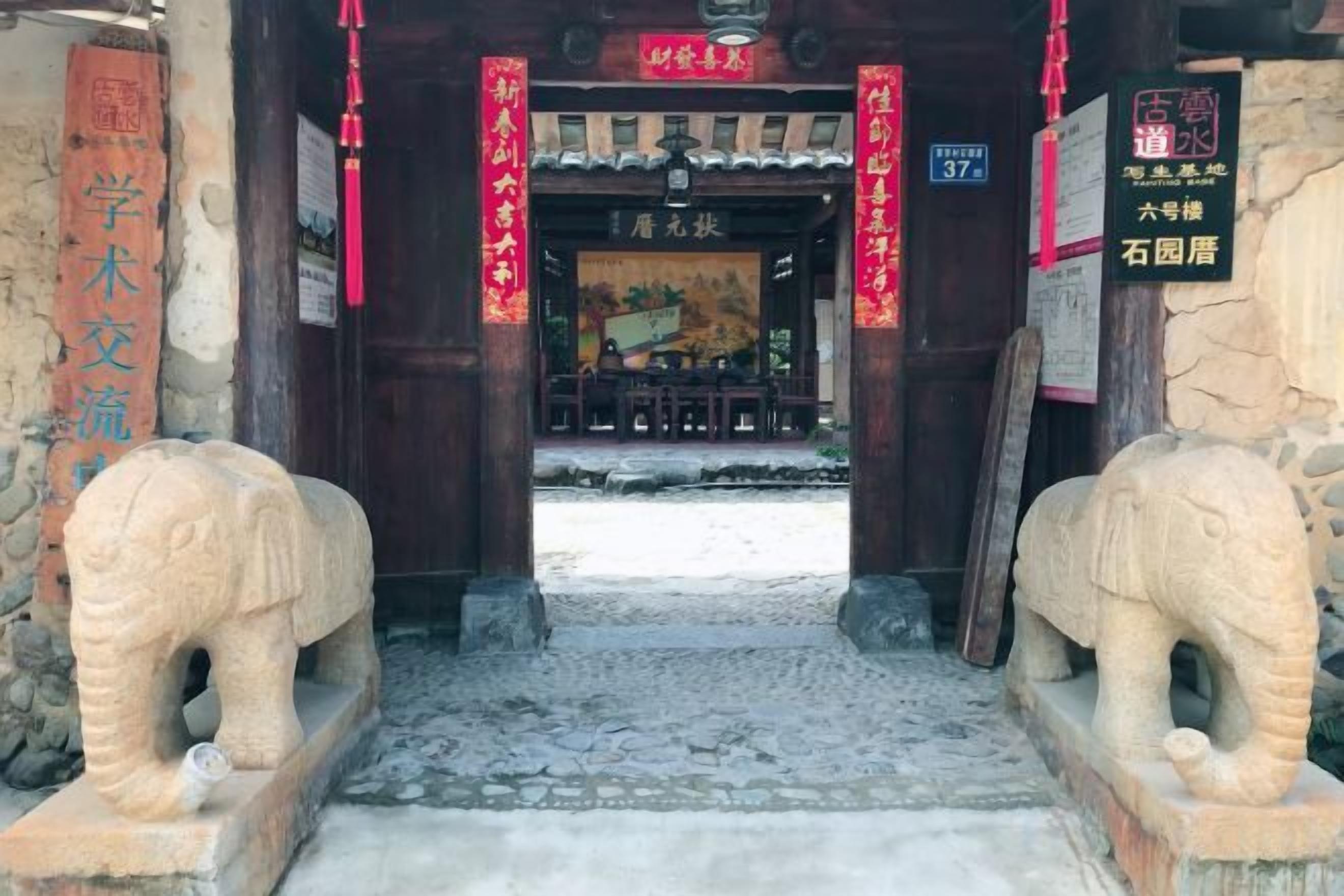 Una puerta tradicional china con elefantes de piedra, un tejado de tejas y un cartel.