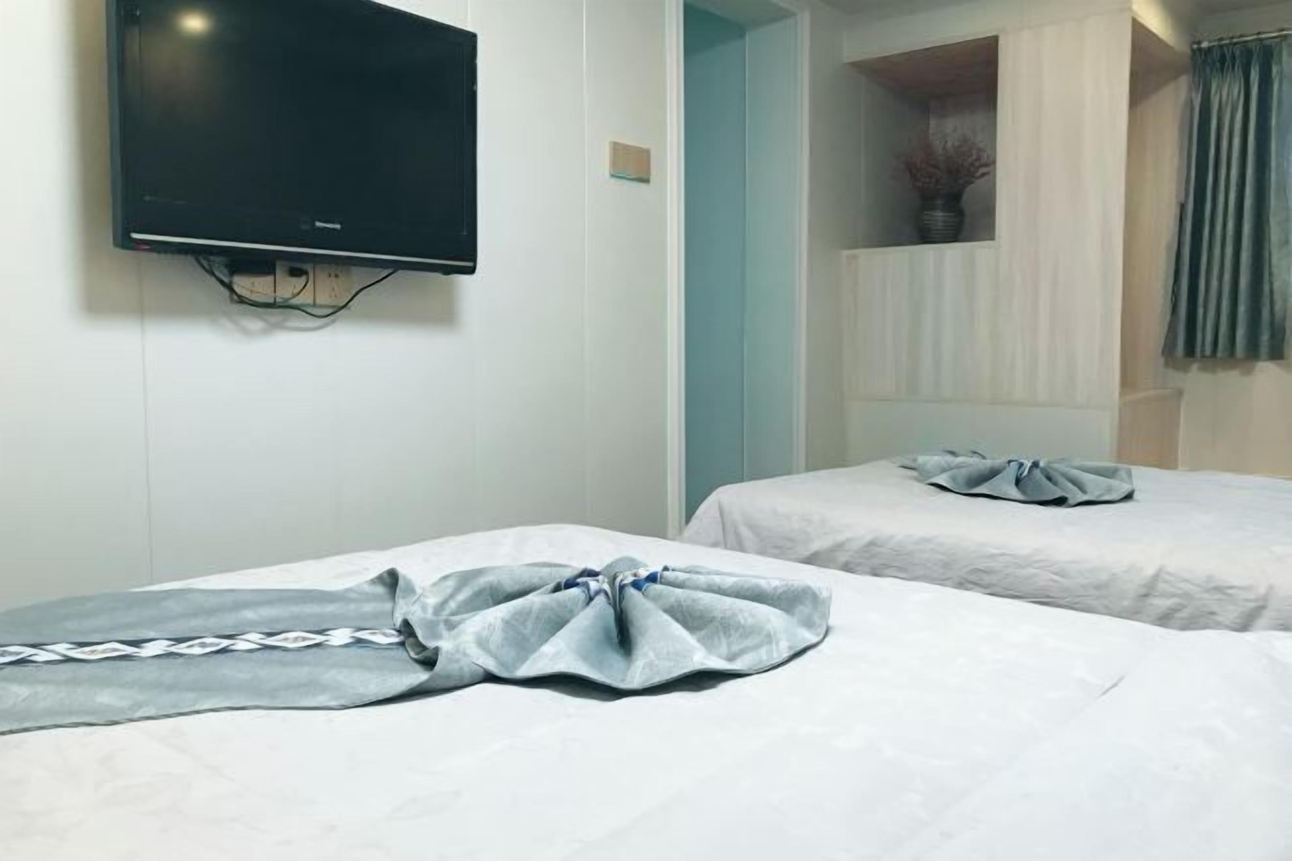A hotel room with two beds, a flat-screen TV mounted on the wall, and a window with curtains.