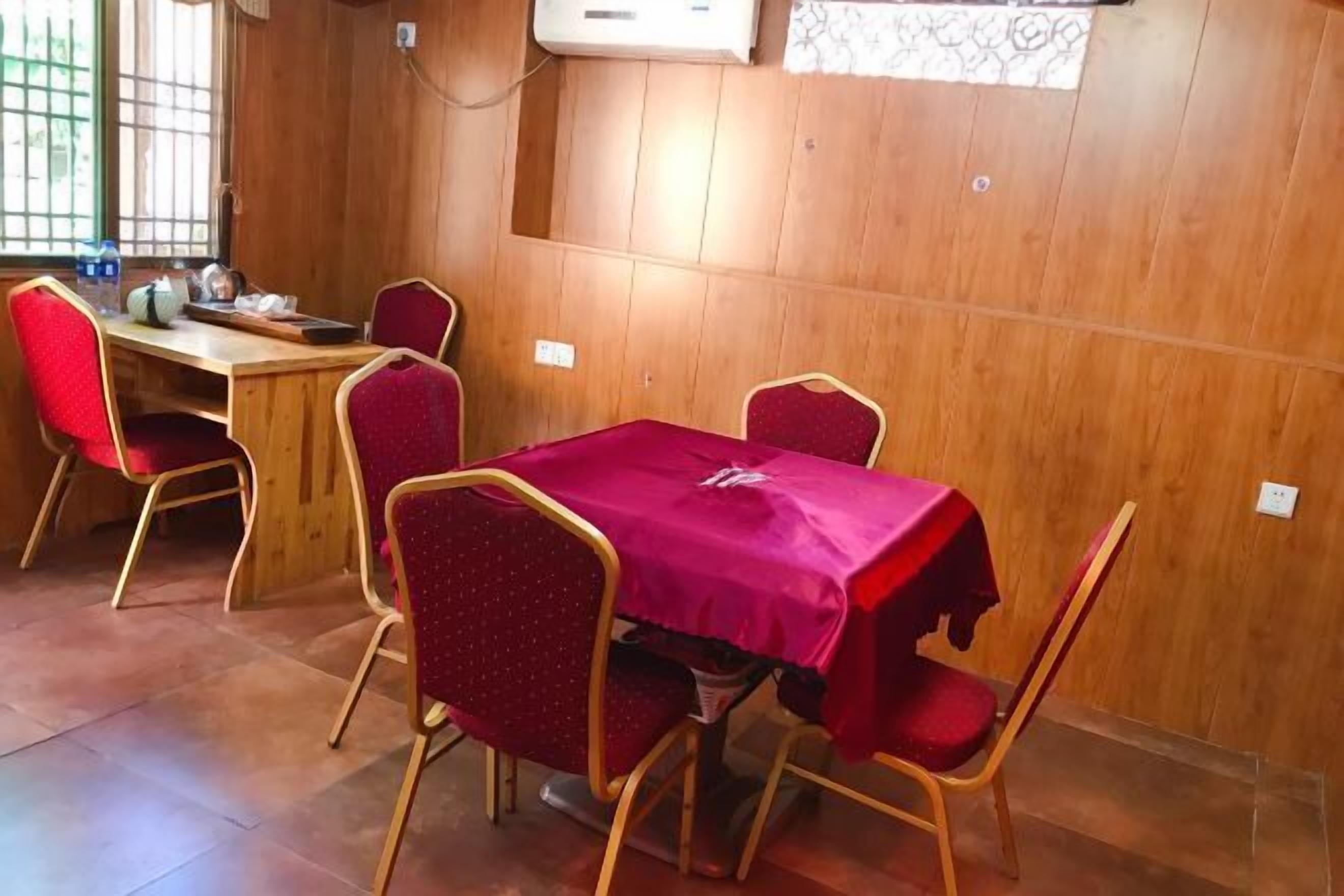 A conference room with a wooden paneled wall, a table covered with a red tablecloth, and four red chairs.