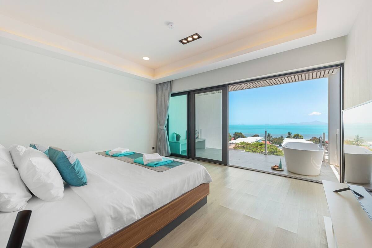 Un dormitorio moderno con una cama grande, vistas al océano y una bañera.