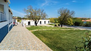 Ein Innenhof mit einem gepflasterten Weg, der zu einem Gebäude mit weißer Fassade und einem kleinen Garten mit Bäumen und Sträuchern führt.