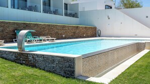 Ein moderner Pool mit Steinwand und Glasgeländern, umgeben von einem gepflegten Rasen.
