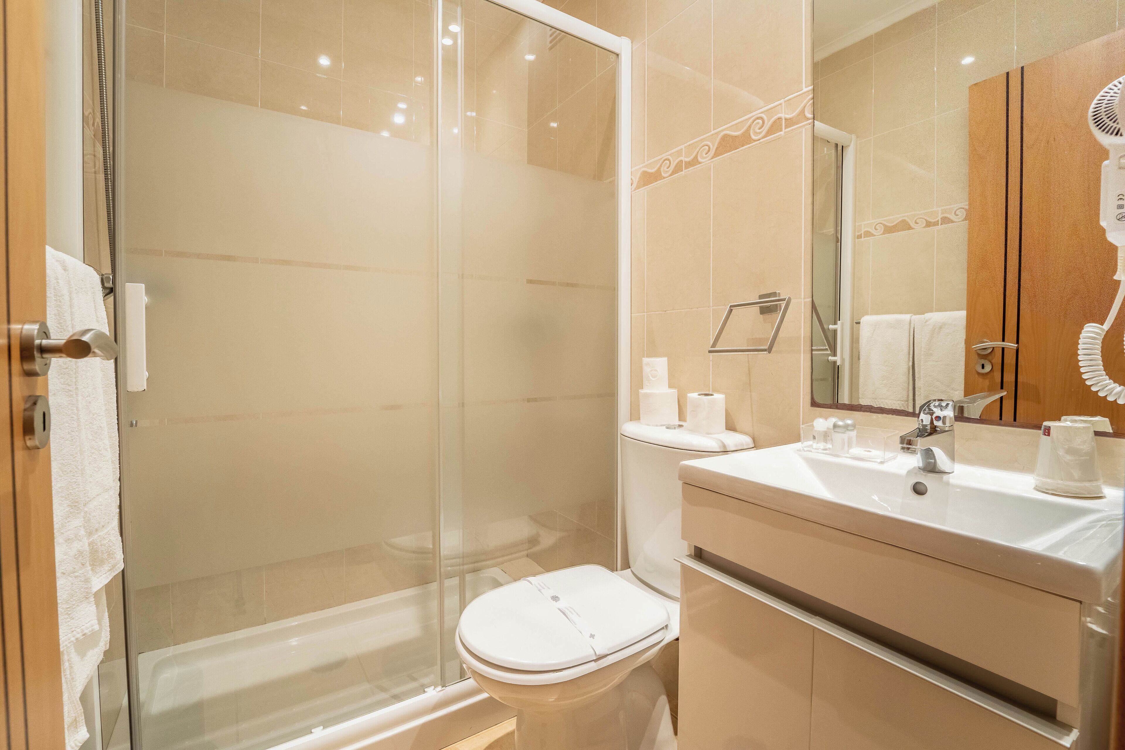 Un baño moderno con ducha de vidrio, inodoro blanco y lavamanos con espejo.