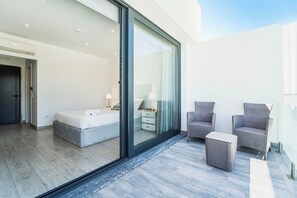 A modern bedroom with a large sliding glass door leading to a balcony, a bed, a nightstand, and two wicker chairs. - Quinta Solar da Portela (Almodôvar)